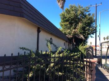 A white building with a dark roof and a black metal fence in front of it.