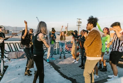 A group of people gathered on a rooftop with graffiti, looking out over a city with mountains in the distance.